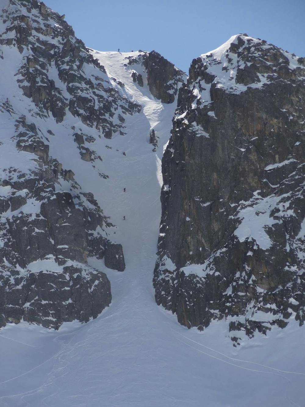 A group of skiers goin down the couloir.