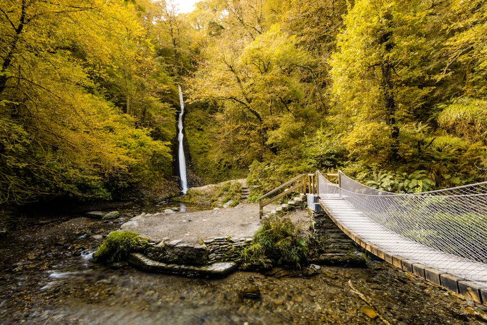 Suspension bridge and waterfall in autumn forest in Lydford Gorge in Devon, UK